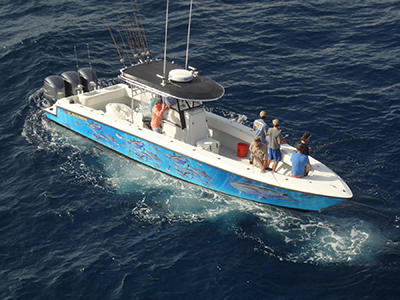 Aerial view of a fishing boat with 7 people on board fishing and painted images of fish on the sides of the boat