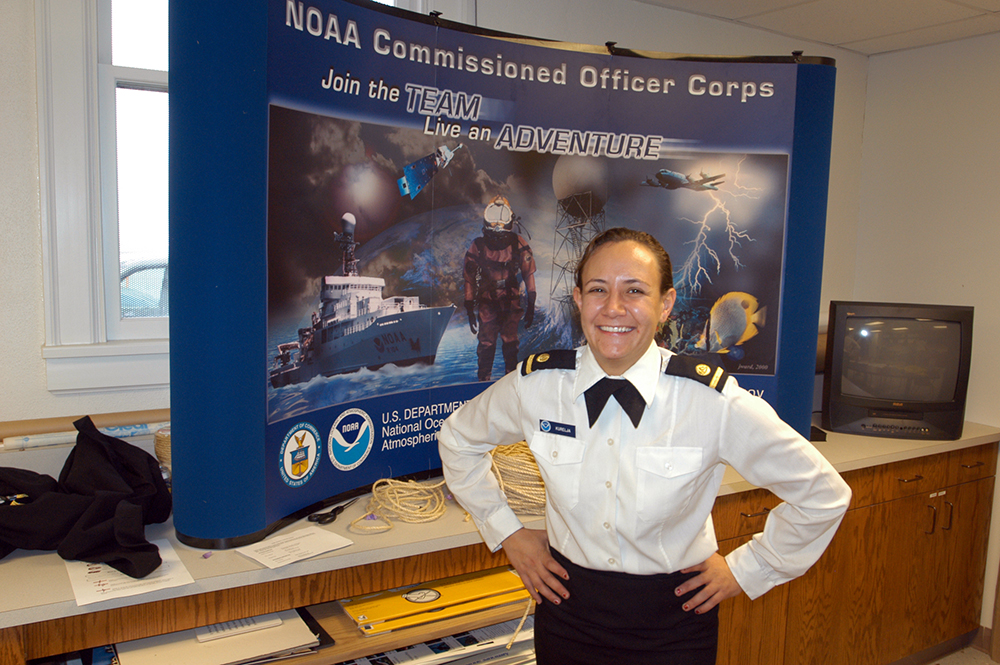 Lindsay in dress uniform standing in front of a table top display about the NOAA Corps.