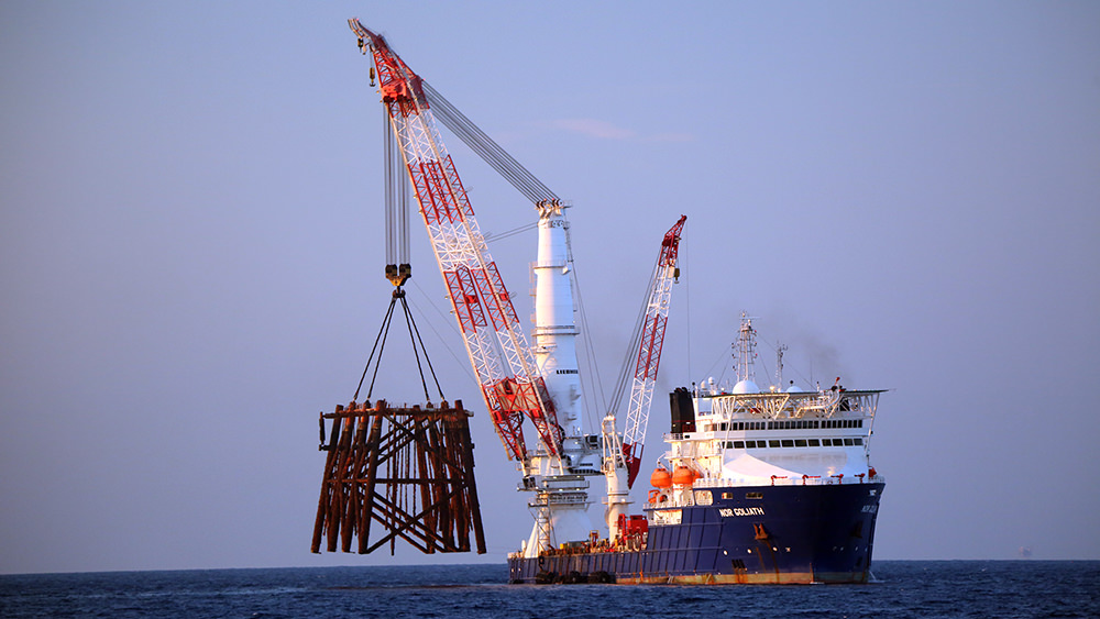 Large ship with crane hoisting the top section of a gas platform out of the water