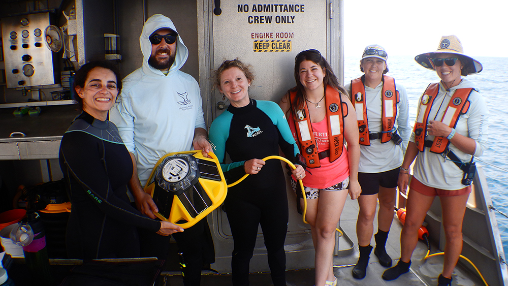 Sanctuary staff holding yellow SoFar buoy and cable on the deck of R/V MANTA